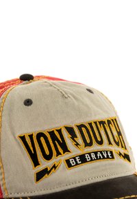 Cappellino multicolore con una parte anteriore color khaki e il testo nero e giallo "VON DUTCH BE BRAVE", cuciture rosse e gialle, e un design arrotondato.