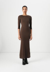 Brown ribbed knit maxi dress with three-quarter sleeves, fitted silhouette, and round neckline, paired with black ankle boots.