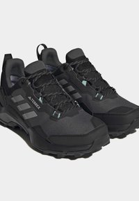 Sorte terrengløpesko med teksturert overdel, forsterkede tær, snøring og yttersåle med dype spor for godt grep. Lyseblå detaljer.