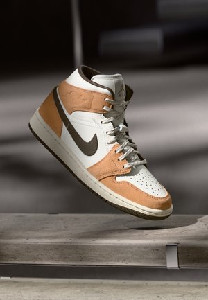 Bežides, valgete ja pruunides toonides kõrged spordijalatsid, millel on Nike Swoosh, paelad ja perforeeritud varvas, rippuvad keset õhku betoonpinna kohal.