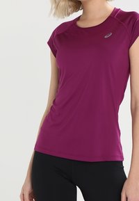 Lila tränings t-shirt med korta ärmar, lättviktig, slät textur, med rund halsringning och en liten logotyp på bröstet.