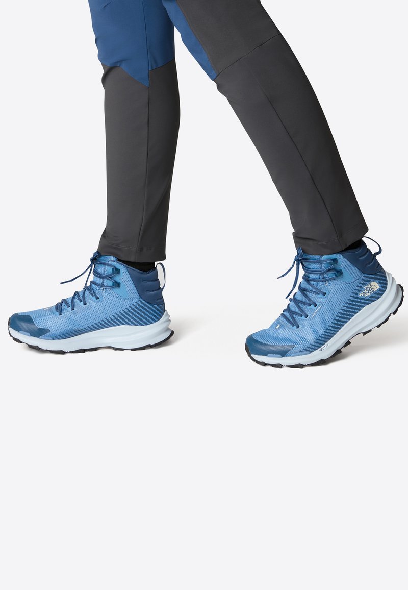 Chaussures de sport bleues avec tige en maille, semelle en caoutchouc et texture détaillée. Design montante avec fermeture à lacets et embout renforcé.