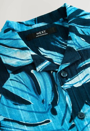 Kurzarmhemd mit einem blauen und schwarzen Blattmuster, aus einem strukturierten Stoff gefertigt, mit einem Knopfverschluss und einem Etikett in der Nähe des Kragens.