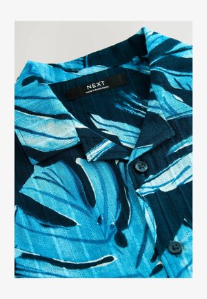 Kurzarmhemd mit einem blauen und schwarzen Blattmuster, aus einem strukturierten Stoff gefertigt, mit einem Knopfverschluss und einem Etikett in der Nähe des Kragens.