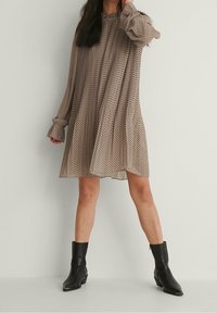 Abito beige a pois con maniche lunghe e larghe, dal taglio rilassato. Abbinato a stivali neri alla caviglia, creando un contrasto di colore e texture.