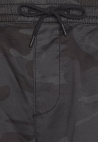 Černé kamuflážové šortky z texturované tkaniny s páskem na stažení v pase. Obsahují boční kapsu s detailem zesíleného švu.