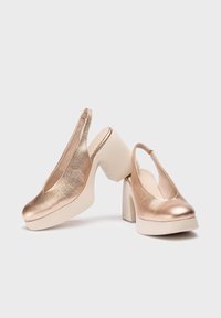 Zapatos de plataforma tipo slingback en color rosado metálico con una superficie texturizada y tacones gruesos en color beige. Punta redondeada, sin patrones o acentos adicionales.