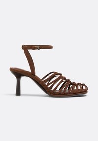Sandale à talons hauts marron avec lanière à la cheville et talon fin incurvé sur fond clair uni.