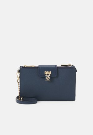 Porte-monnaie bracelet en cuir bleu marine avec fermeture éclair dorée, bandoulière chaîne et détail serrure sur le rabat avant.