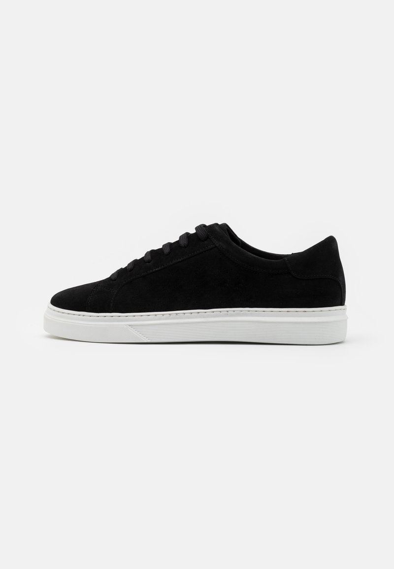 Baskets basses noires avec dessus en daim, lacets noirs et semelle en caoutchouc blanche, vues de côté sur fond blanc.