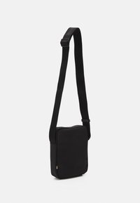 Borsa a spalla nera realizzata in tessuto resistente. Caratterizzata da una forma quadrata, tracolla regolabile e un piccolo dettaglio con logo sul lato. Texture liscia.