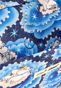 Tessuto blu con stampa Moomin che presenta personaggi su nuvole, accenti a forma di stelle e uno sfondo blu scuro con un aspetto testurizzato. Etichetta del tessuto inclusa.