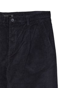 Pantaloni in corduroy blu scuro con chiusura a bottone, passanti per cintura e tasche laterali inclinate, etichettati con tag di misura e marca all'interno della vita.