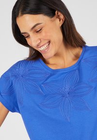 T-shirt blu con ricami floreali in una texture leggermente in rilievo, con grandi design floreali sul davanti e scollo rotondo.