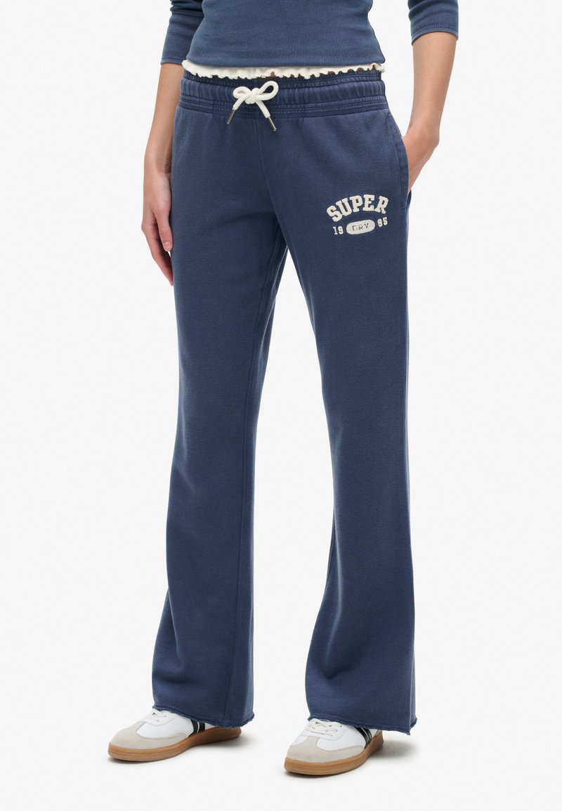 Marineblå sweatpants lavet af blødt stof, med snor i livet og hvidt trykt tekst "SUPER 1985" på venstre lår.