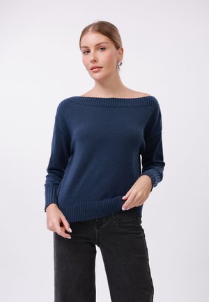 Mørkeblå genser med bred off-shoulder halslinje, ribbede mansjetter og kant, teksturert strikket stoff, sammen med svarte bukser.