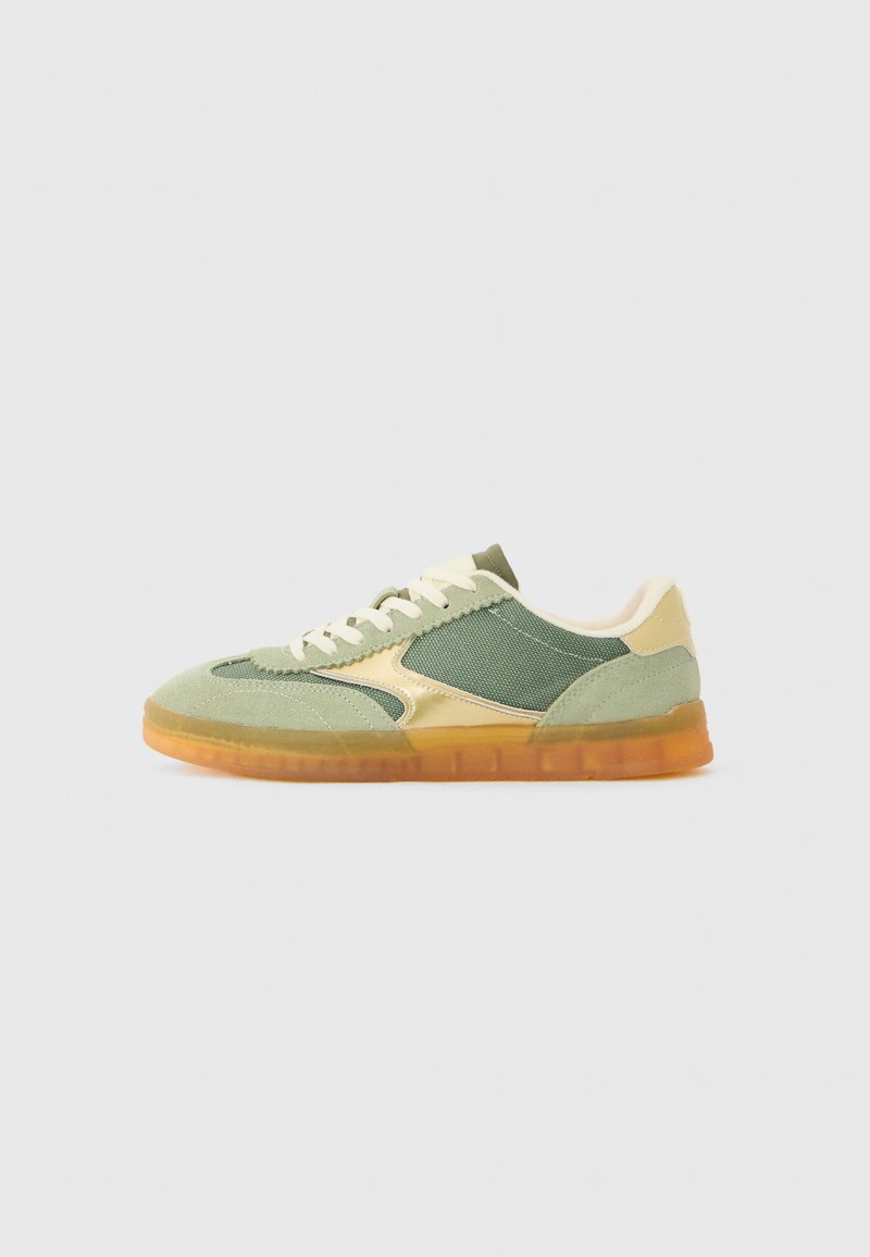 Grønne og gule joggesko med overdel i nubuck og mesh, gullakenter og en gjennomsiktig oransje såle. Har hvite snøring og broderte detaljer.