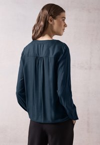 Dunkelblaugrüne Bluse mit langen Ärmeln, einem subtilen Texturmuster, rundem Halsausschnitt, Falten-Detail am Rücken und leicht gerafften Ärmeln.