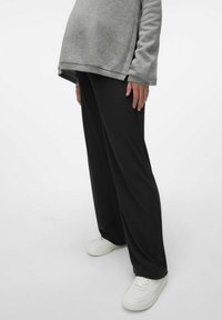 Pantalons larges à côtes noirs en tissu doux avec une taille haute, associés à des baskets blanches et un haut gris.