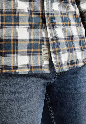 Koszula w kratę w kolorach niebieskim, białym i żółtym, wykonana z materiału o gładkiej fakturze. Metka widoczna na boku, zestawiona z ciemnoniebieskimi dżinsami.