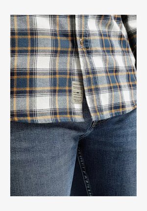 Koszula w kratę w kolorach niebieskim, białym i żółtym, wykonana z materiału o gładkiej fakturze. Metka widoczna na boku, zestawiona z ciemnoniebieskimi dżinsami.