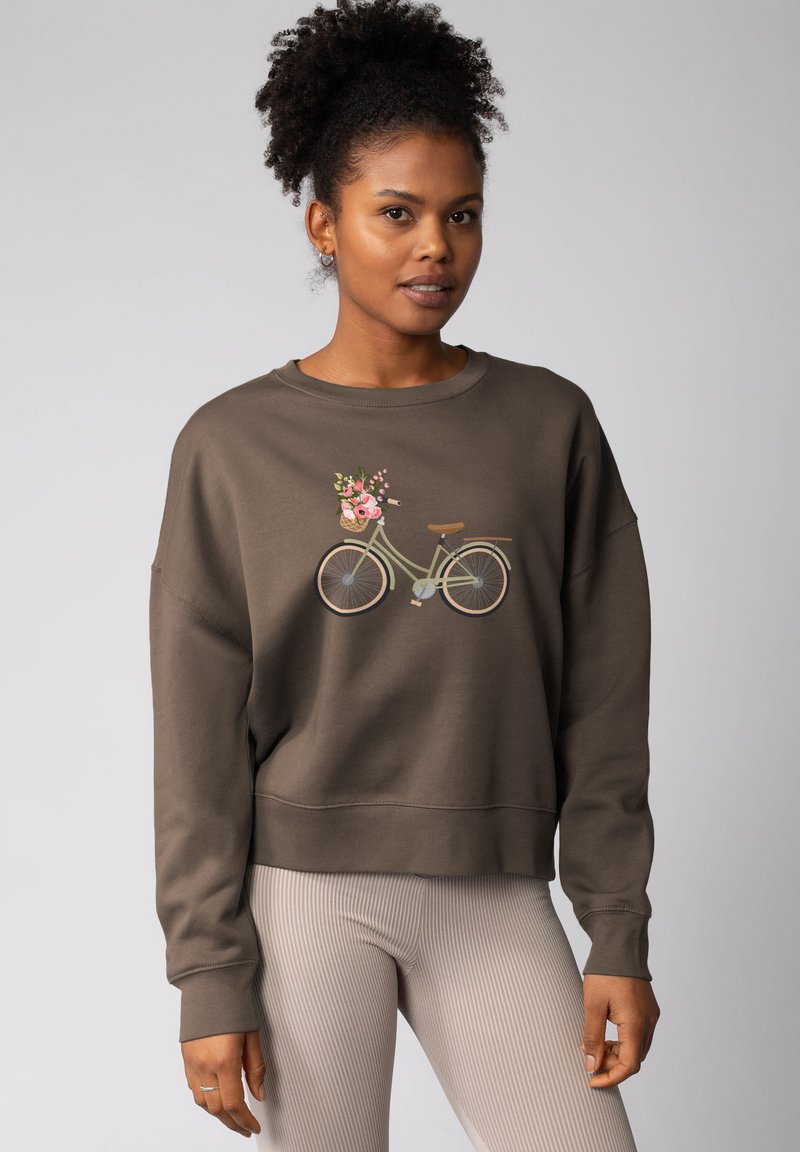Bruine sweatshirt met een fietsafbeelding met een bloemenmand. Ribgebreide manchetten en zoom, ontspannen pasvorm, gecombineerd met ribgebreide lichtgekleurde leggings.