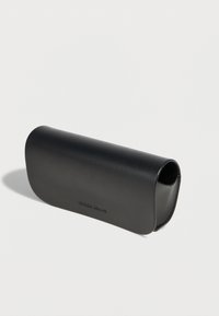 Estuche rígido para gafas de Giorgio Armani en color negro con logo en relieve, ligeramente abierto, sobre un fondo liso claro.