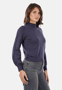 Maglione a manica lunga blu navy con collo alto, design aderente e polsini a coste. Texture liscia, stile minimalista, senza fantasie.