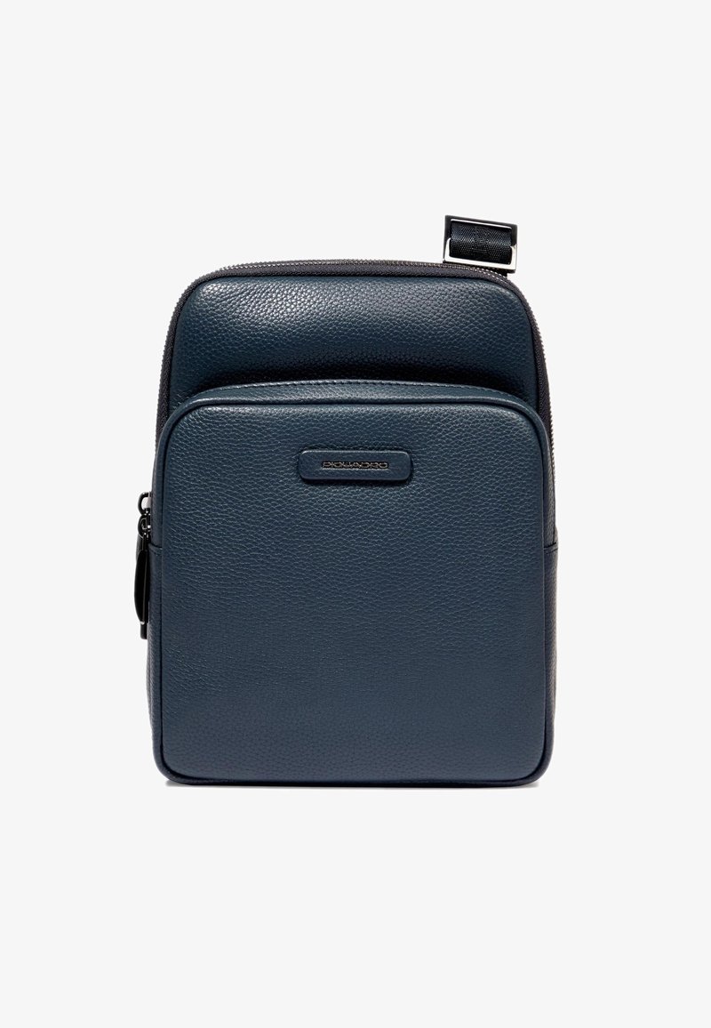 Zaino in pelle blu navy con texture a grana, forma rettangolare, tasca frontale con cerniera e branding discreto su una sottile linguetta orizzontale.