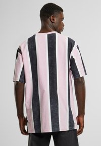 Vertical striped t-shirt in pink, dark gray, and white. Cotton material with a relaxed fit and short sleeves. Crew neckline, contrasting colors.