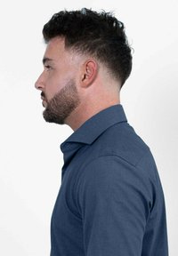 Marinblaues Hemd mit strukturiertem Kragen und langen Ärmeln. Der Stoff erscheint glatt und texturiert, hat eine taillierte Passform und klare Linien.