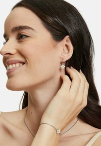 Silverörhängen med ett blommönster som har fyra vita stenar, kompletterade med ett matchande armband och ett enkelt halsband.