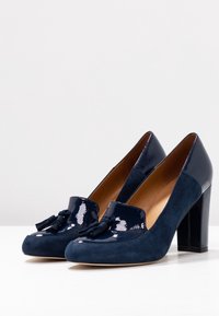 Scarpe con tacco alto blu navy con punta piatta, in materiale scamosciato e verniciato, e un fiocco decorativo sul davanti. Finitura texturizzata sui tacchi.