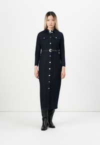 Robe chemise en denim bleu marine, avec des manches longues, deux poches poitrine, des boutons sur le devant, une taille ceinturée et une coupe droite.