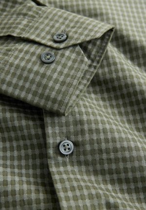 Žalia ir pilka languota marškinėliai su tekstūruota medžiaga, turintys du pilkus sagas ant rankogalių ir smailų apykaklės dizainą.