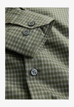 Grün-grau kariertes Hemd aus strukturiertem Stoff, mit zwei grauen Knöpfen an den Manschetten und einem spitzen Kragen.