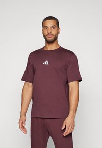Burgundi színű, rövid ujjú pamut póló, melyen egy finom, fehér és szürke gradiens Adidas logó található. Puha tapintású és laza fazonú.
