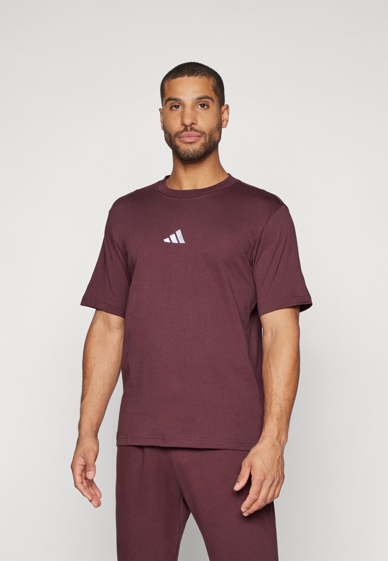 Burgundi színű, rövid ujjú pamut póló, melyen egy finom, fehér és szürke gradiens Adidas logó található. Puha tapintású és laza fazonú.