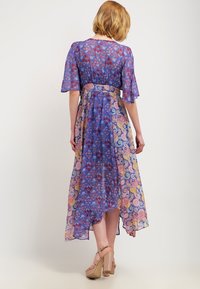 Maxi šaty z modré průhledné látky s květinovými a paisley vzory, krátkými rukávy a pásem v pase. Spodní lem je delší na zadní straně.