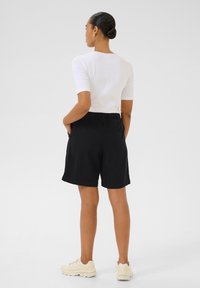 Shorts noirs avec une taille élastique et des poches latérales, associés à un haut ajusté à manches courtes blanc. L'arrière-plan est entièrement blanc.