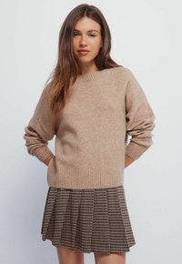 Maglione beige lavorato a maglia con polsini e orlo a coste, abbinato a una gonna plissettata a fantasia in toni scuri e chiari. Texture liscia.