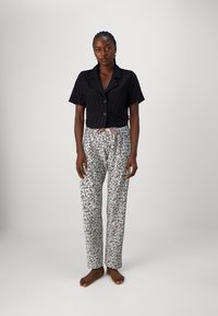 Zwart kort verborgen shirt met knoopsluiting, gecombineerd met losse witte broek met een kleurrijk bladerpatroon en een trekkoord in de taille.