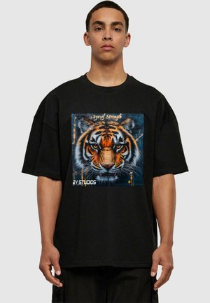 Black oversized t-shirt featuring a colorful tiger graphic with the text "Eye of Strength" and "2Y STUDIOS" at the bottom.
