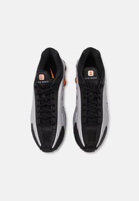 Černé a stříbrné sportovní boty s elegantním designem, které mají texturovanou látku, zaoblenou špičku a oranžové detaily na patě a podrážce.