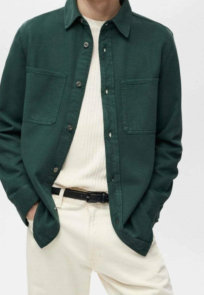 Chemise boutonnée vert foncé en coton, avec deux poches poitrine, un col pointu et une coupe décontractée, associée à un pull clair à côtes.