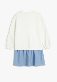 Hvid sweatshirt med lange ærmer, buet kant, lagdelt over lyseblå stribet stof, hvilket skaber en flagrende bund.