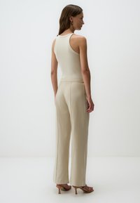 Canottiera a coste beige abbinata a pantaloni a gamba larga beige chiaro, caratterizzati da una texture liscia e tasche laterali sottili, vista da dietro.