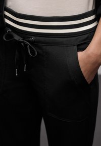 Schwarze Jogginghosen mit einem gestreiften elastischen Bund und Kordelzug, Seitentaschen und einer glatten Textur.