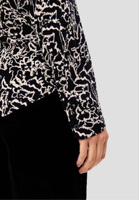 Camicia a maniche lunghe con un motivo astratto in bianco e nero, tessuto texturizzato e polsini con bottoni, abbinata a pantaloni in velluto a coste scuri.