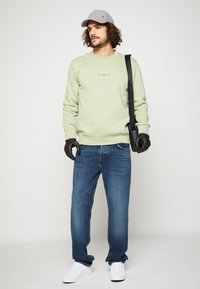 Lysegrønn genser med rund hals, blå jeans og hvite sneakers. En grå caps og svarte hansker fullfører antrekket, sammen med en skulderveske.